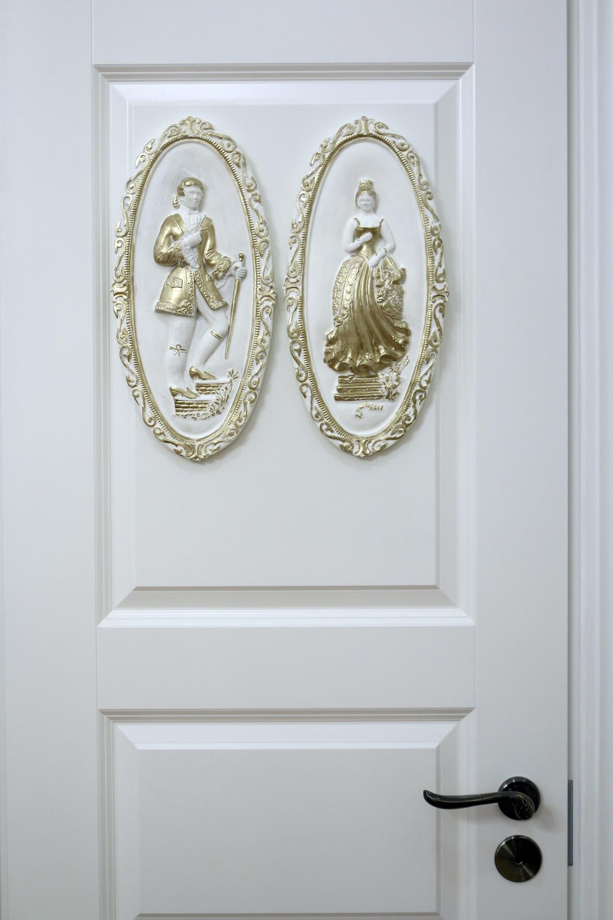 Pair of oval wall plaques with a cavalier and a lady in gilded frames mounted on a white door