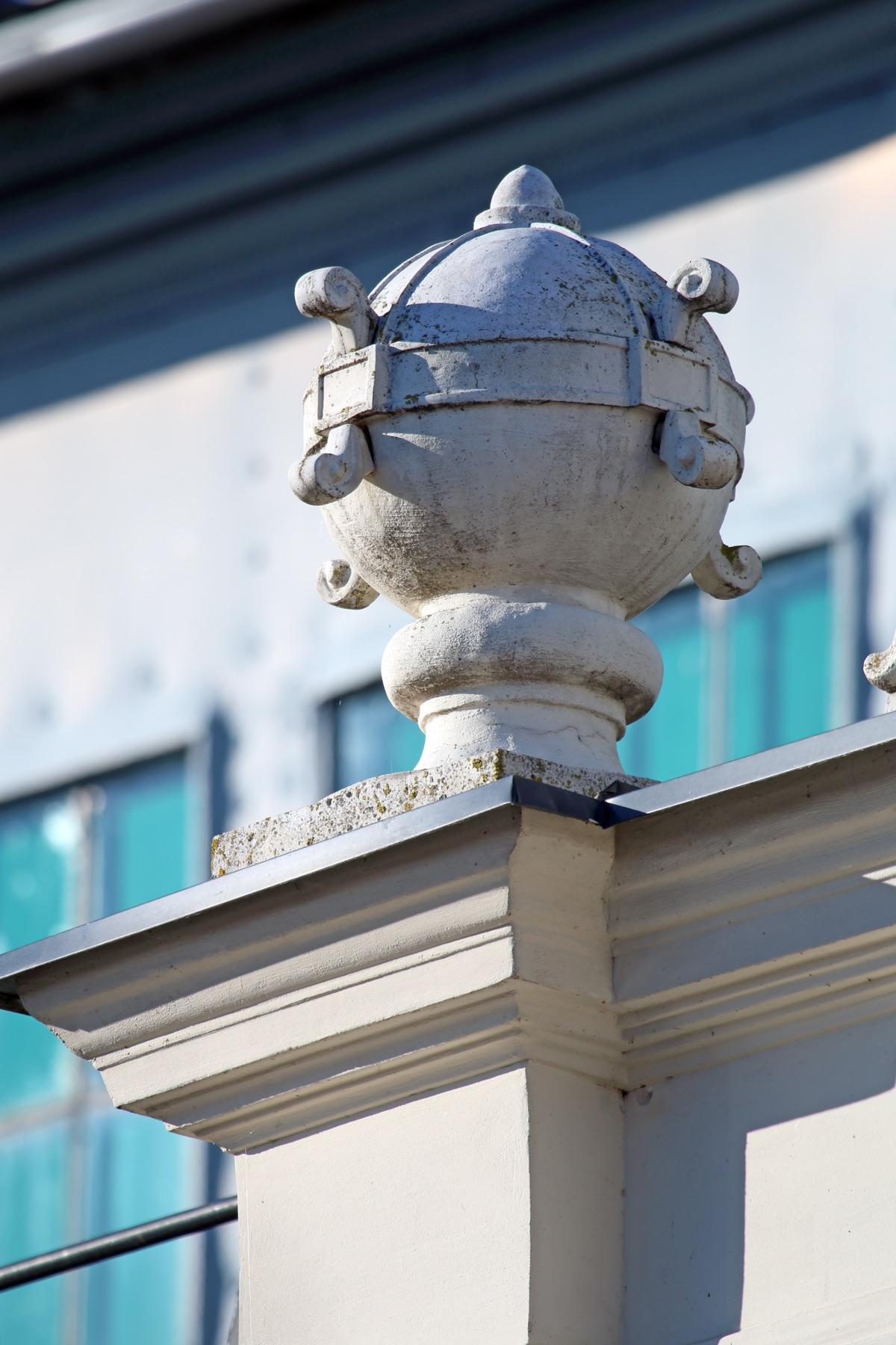 Spherical plaster acroterion with volutes on a building corner pedestal