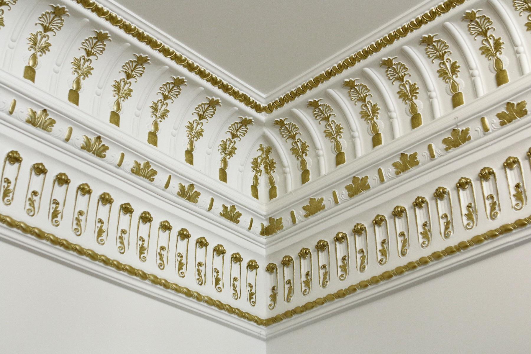 Corner of an Empire-style ceiling cornice with gilded palmettes in arched niches, freshly installed